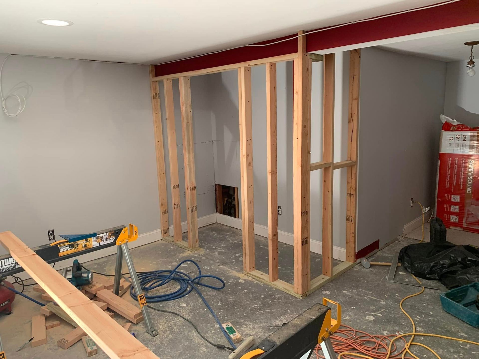 Construction site with wooden framing for a room, gray walls, tools and materials scattered on the floor.