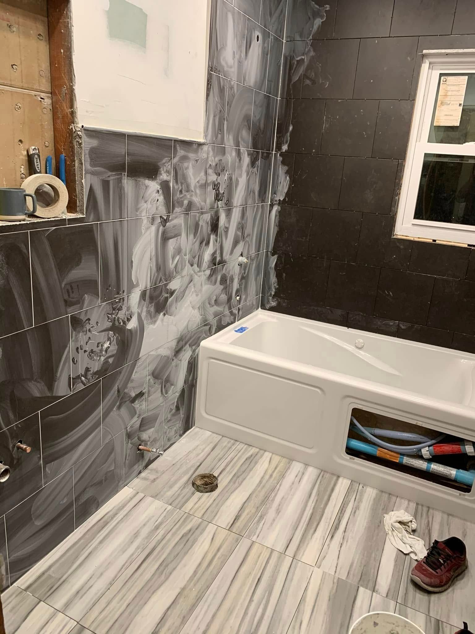 Bathroom under construction with tub, partially tiled walls, and light-colored floor.