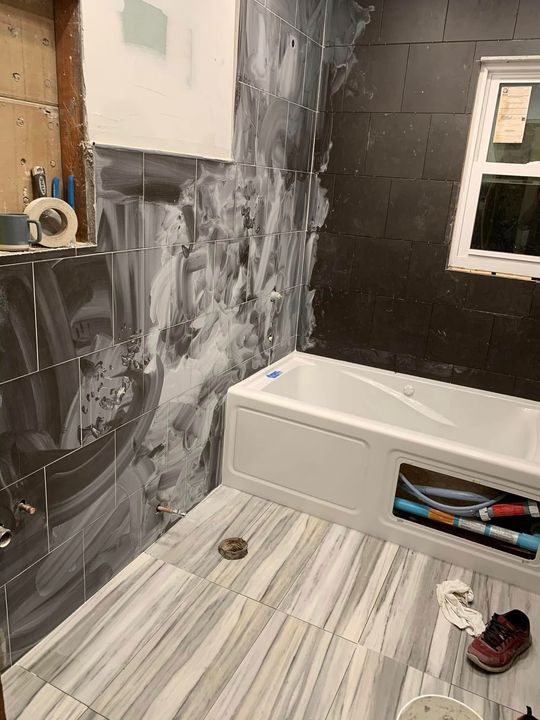 Bathroom under construction with tub, partially tiled walls, and light-colored floor.