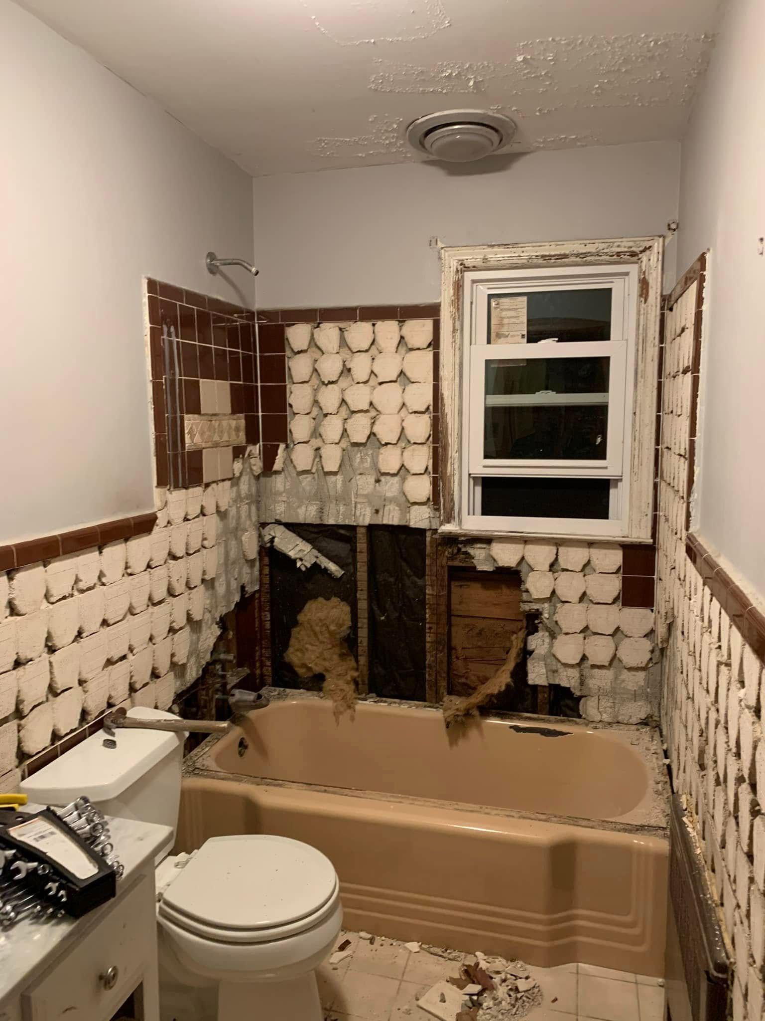 Bathroom in disrepair with exposed walls, pink tub, and brown and white tiles.