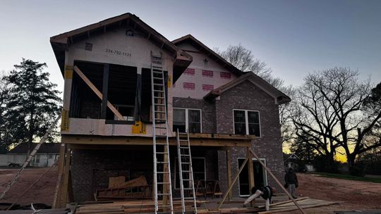 House under construction; brick and wood exterior, scaffolding and ladders, overcast sky.