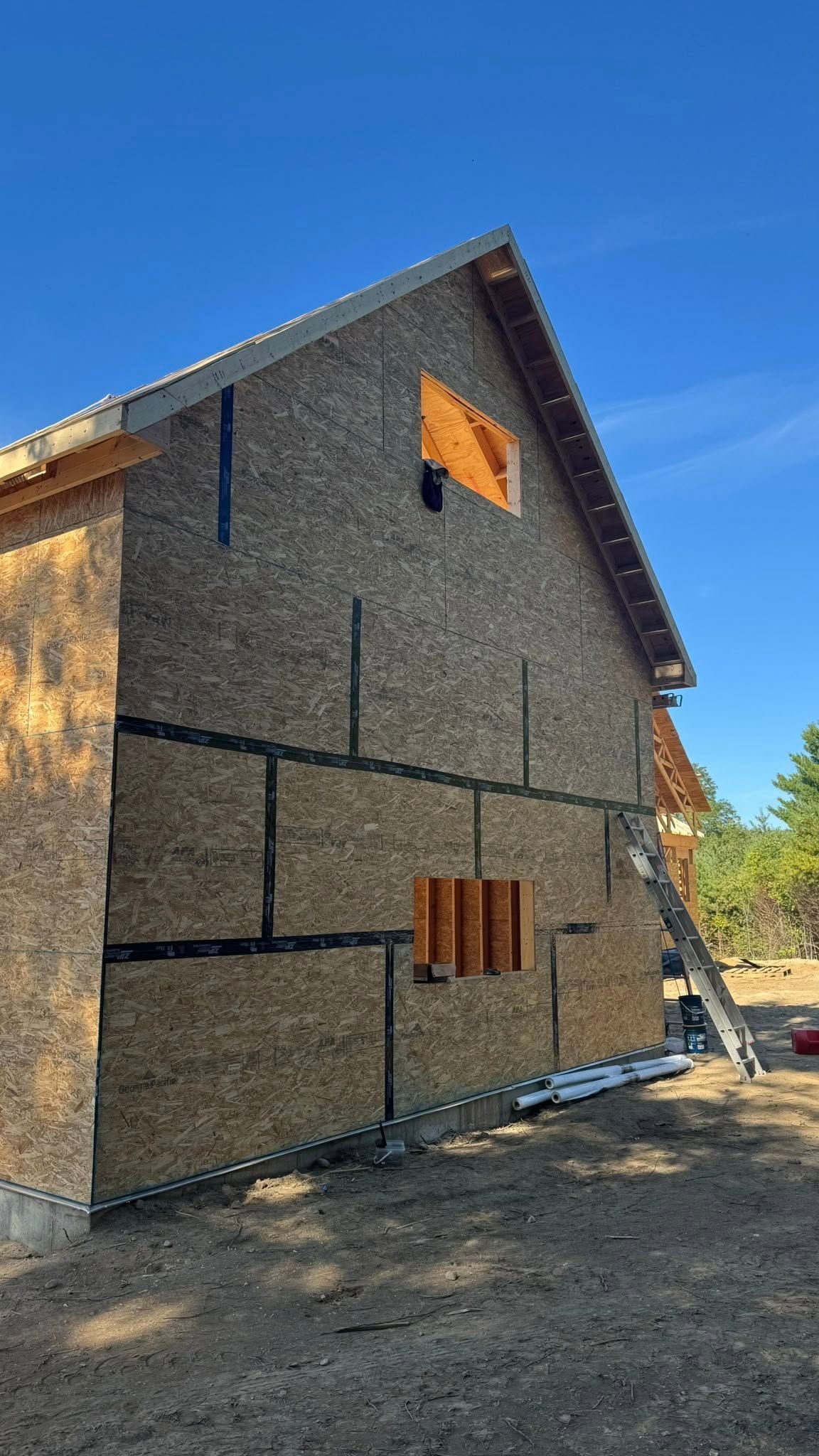Exterior of a building under construction. Brown siding, black tape, with a ladder leaning against the wall.