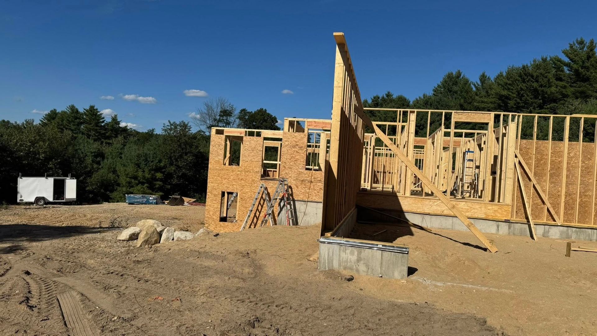 House under construction, wooden frame with OSB sheathing against a blue sky.