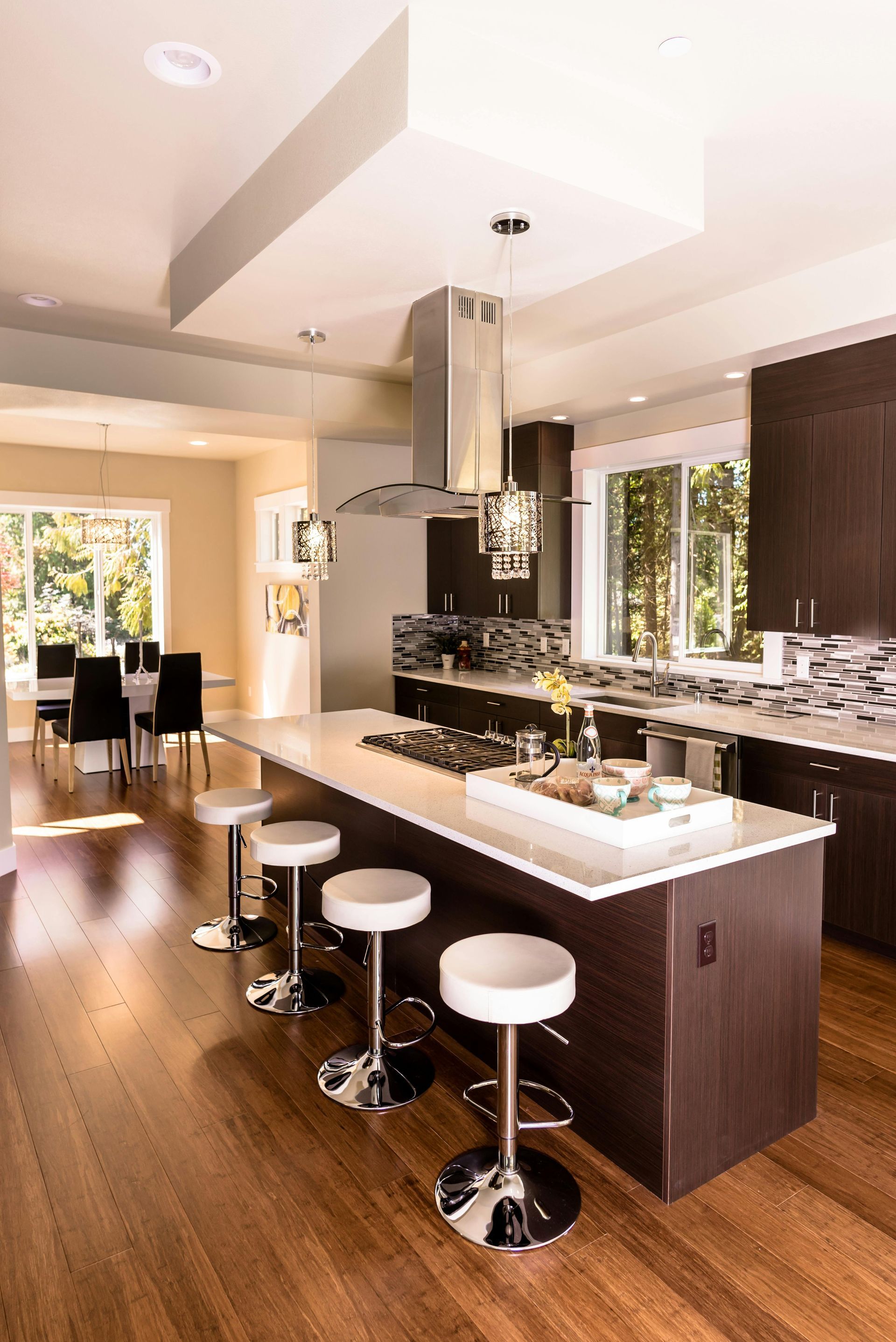 Modern kitchen with dark wood cabinets, white island, bar stools, and stainless steel range hood