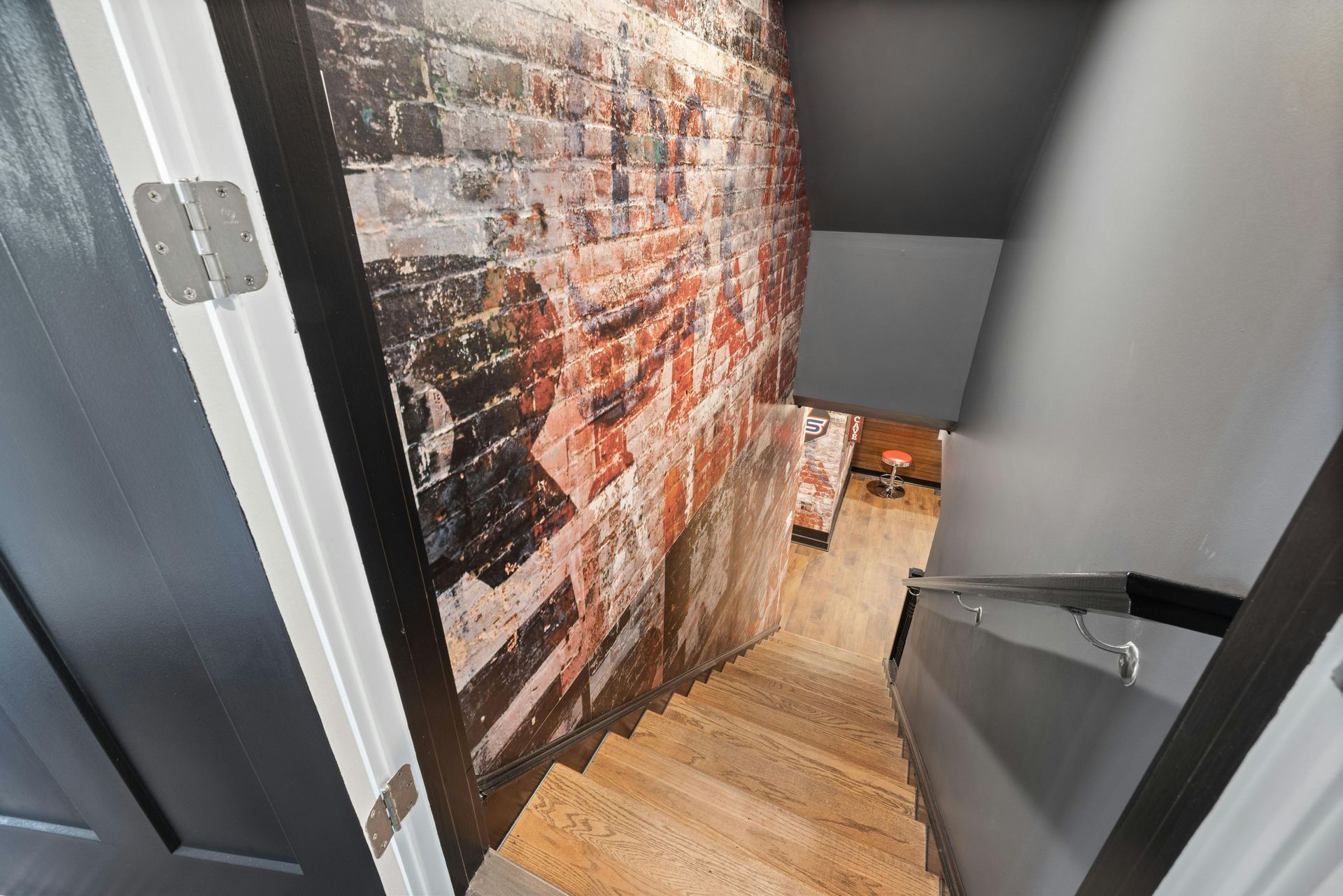 Stairwell with wooden steps, gray walls, and a brick mural along the left side.