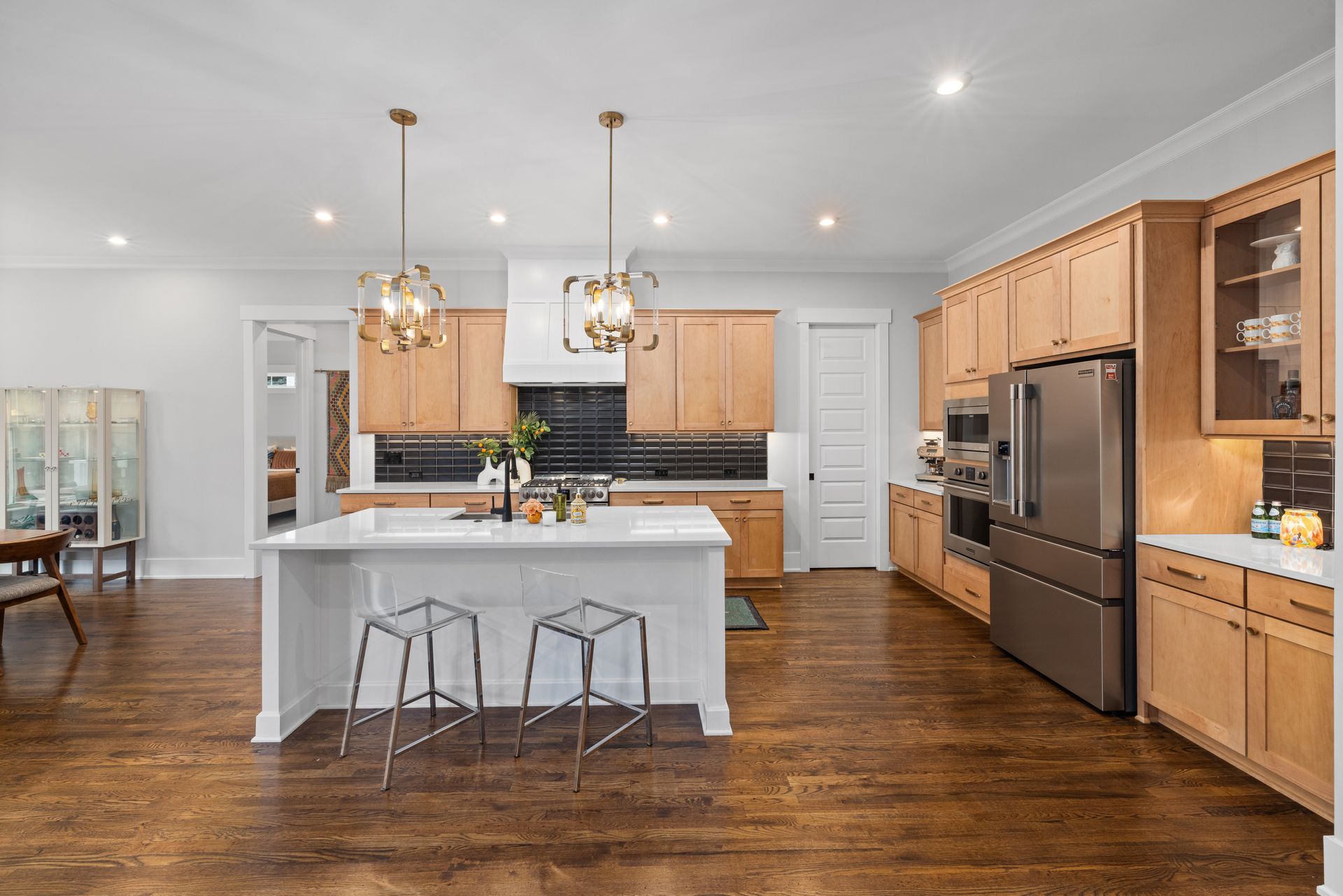 Bright modern kitchen with a white island, wood cabinets, stainless fridge, and hardwood floors