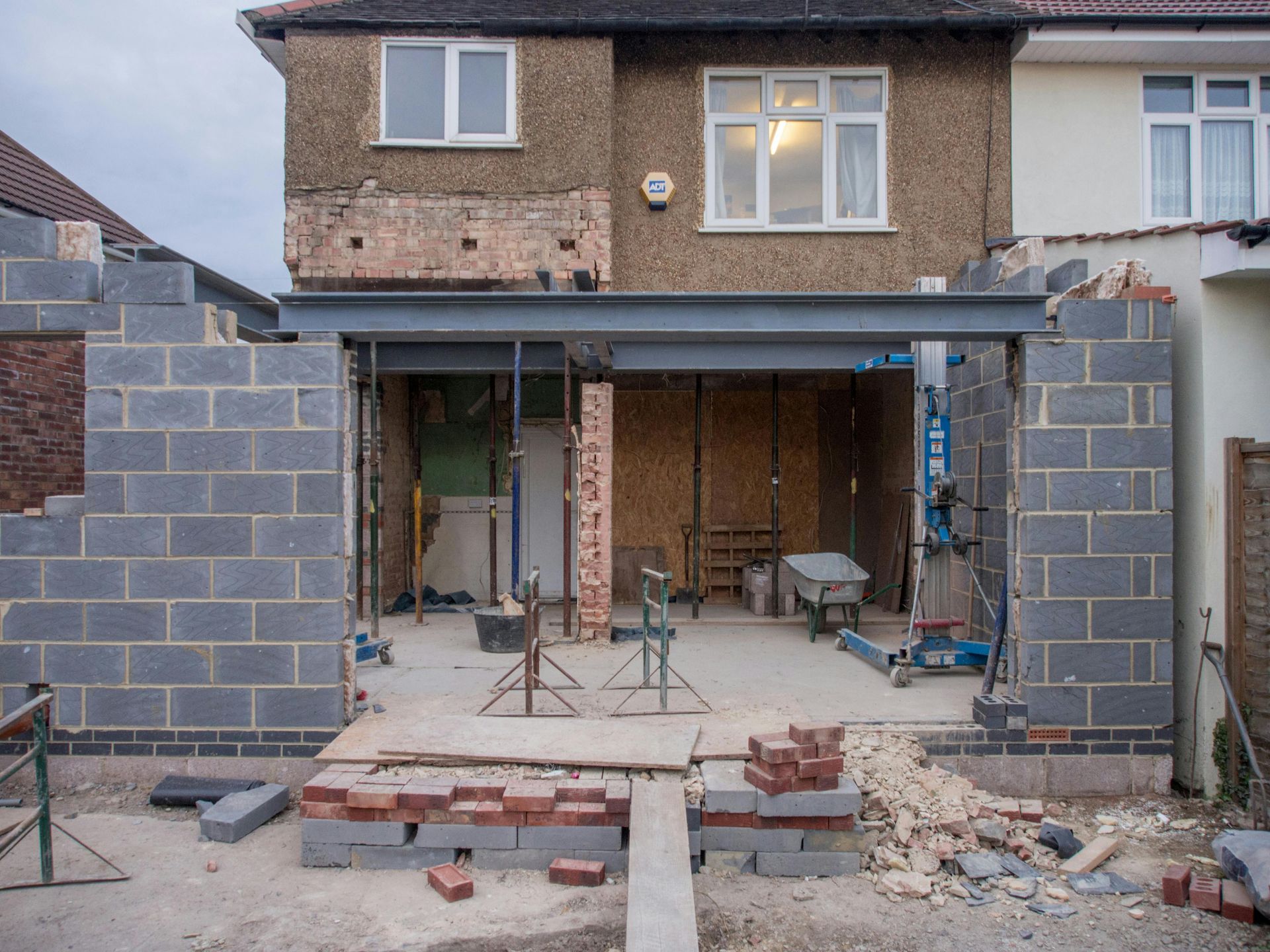 House front under construction with open garage, scaffolding, and partially built brick walls