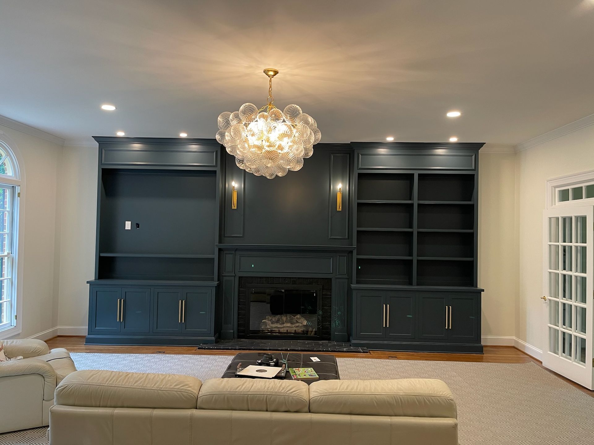 A living room with a fireplace, couch, shelves and a chandelier.