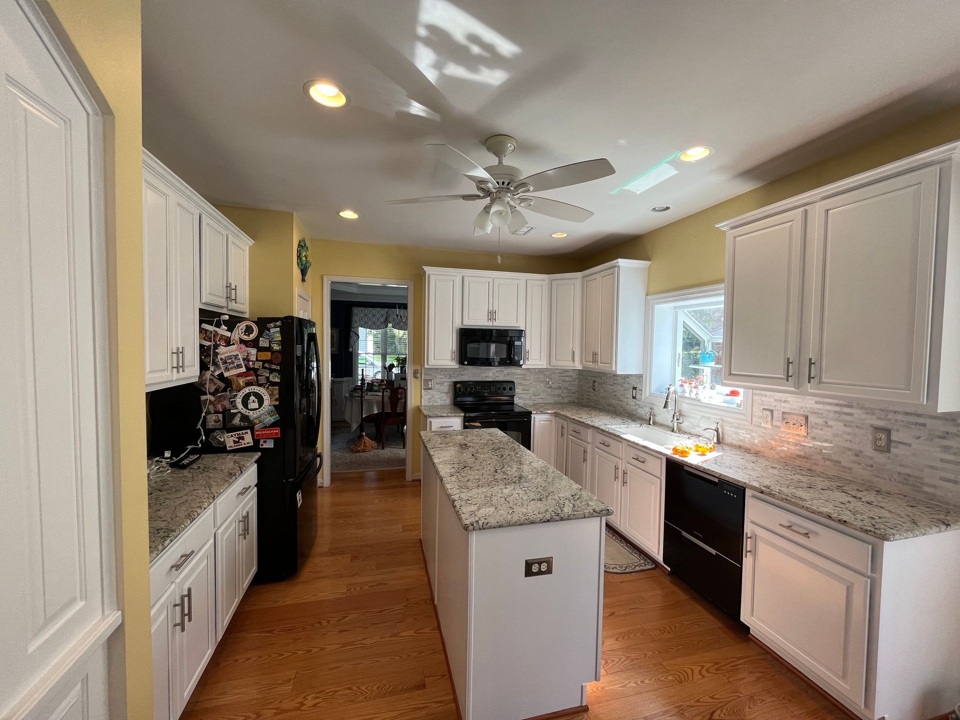 A kitchen with white cabinets, granite counter tops, and a ceiling fan.