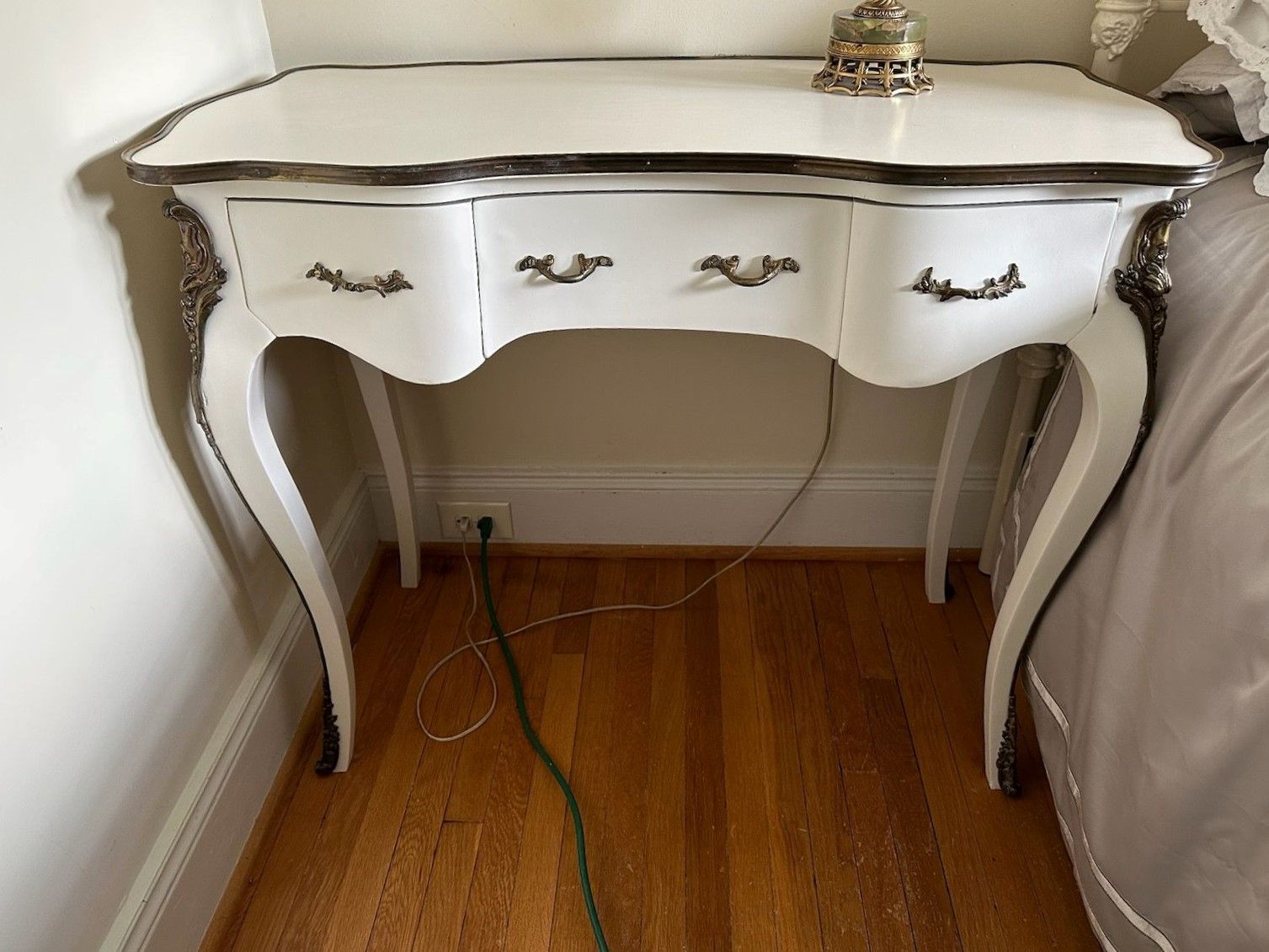 A white table with three drawers is in a bedroom next to a bed.