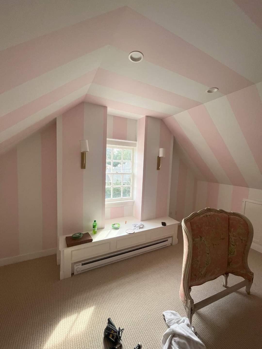 A bedroom with pink and white stripped walls, a couch, and a window.