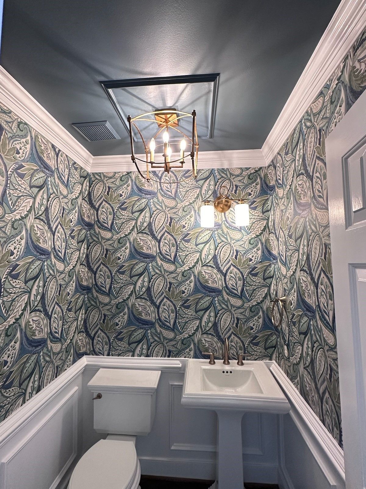 A bathroom with a toilet, sink, and chandelier.