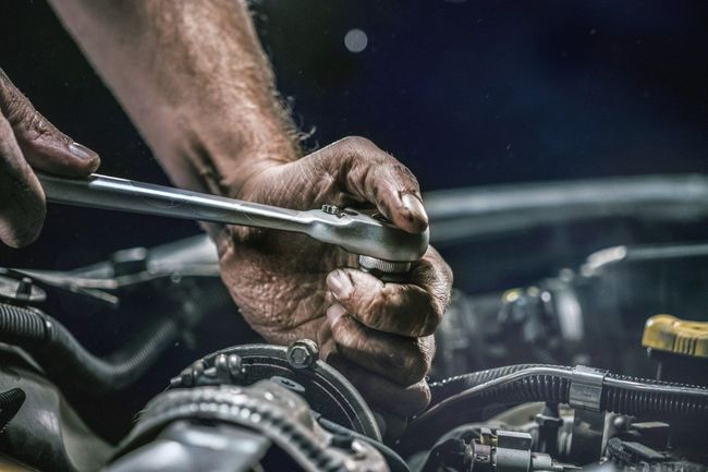 Mechanic's hands using a wrench to work on a car engine. The hands are dirty, likely indicating the process is messy.