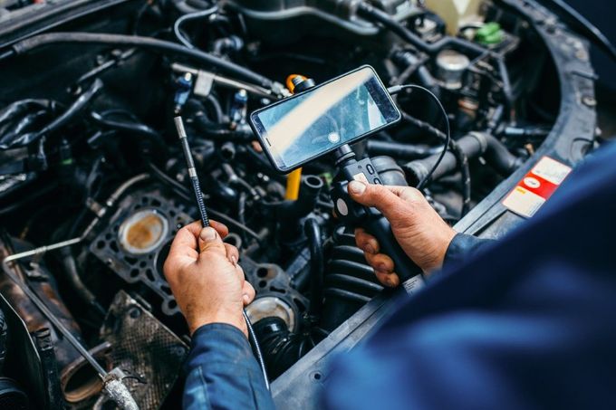 Mechanic inspecting a car engine with a bore scope, revealing internal components; blue uniform.