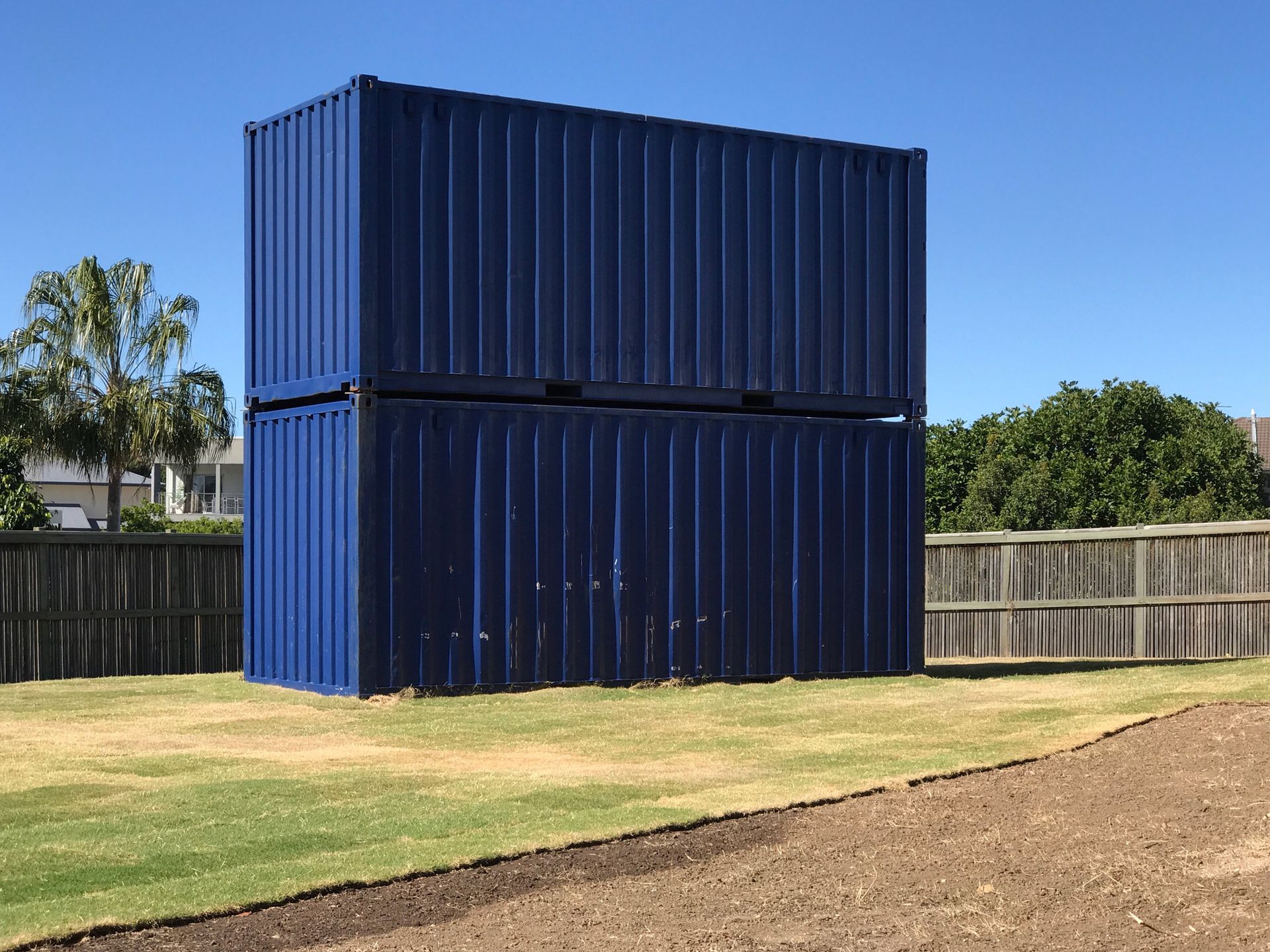 Two blue shipping containers are stacked on top of each other in a grassy field.