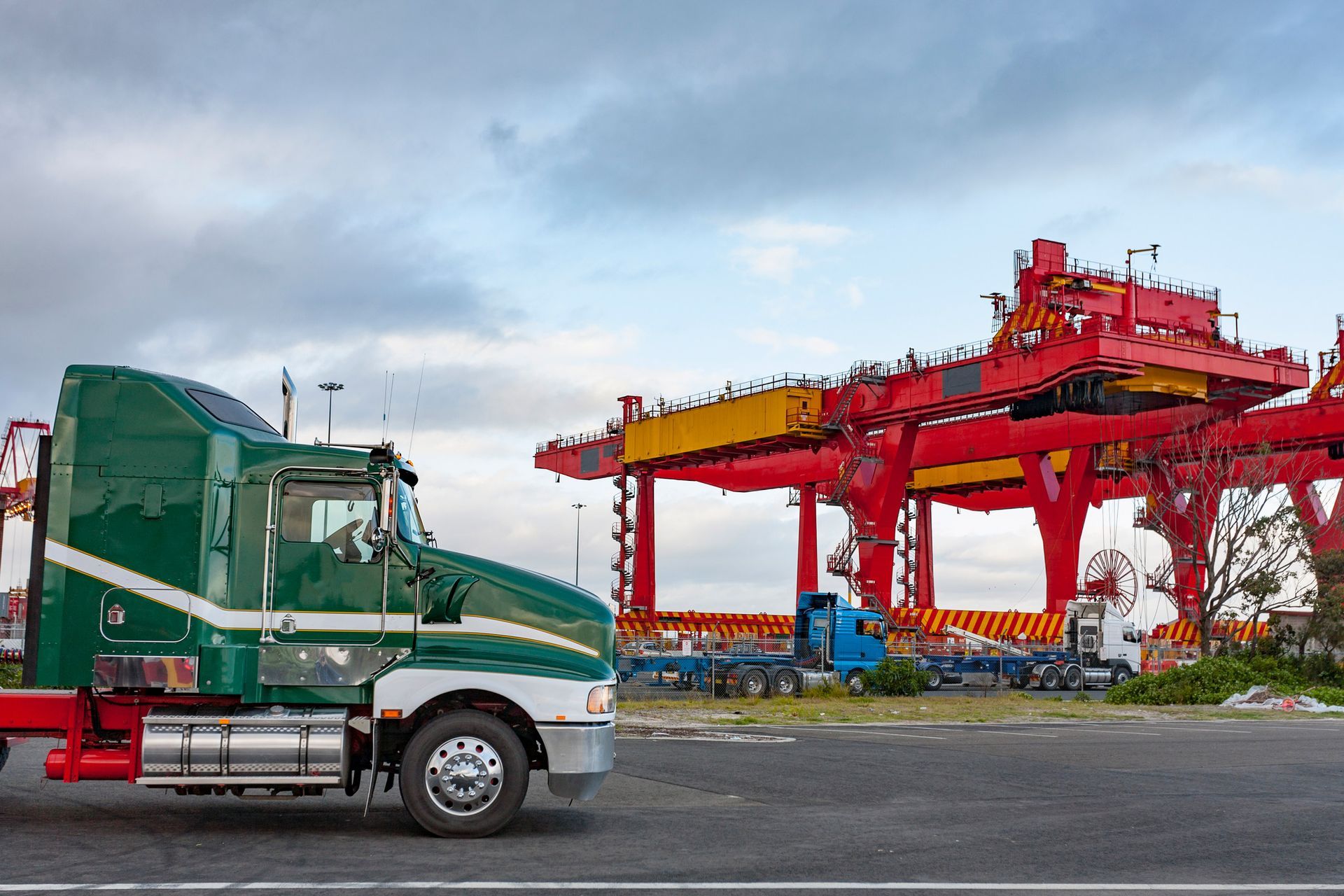 A green semi truck is parked in front of a large crane.