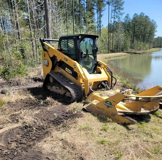 Yellow Caterpillar skid steer with brush cutter attachment near a pond, clearing land.