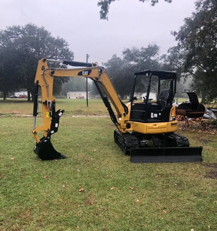 Yellow Caterpillar mini excavator on green grass under a cloudy sky.
