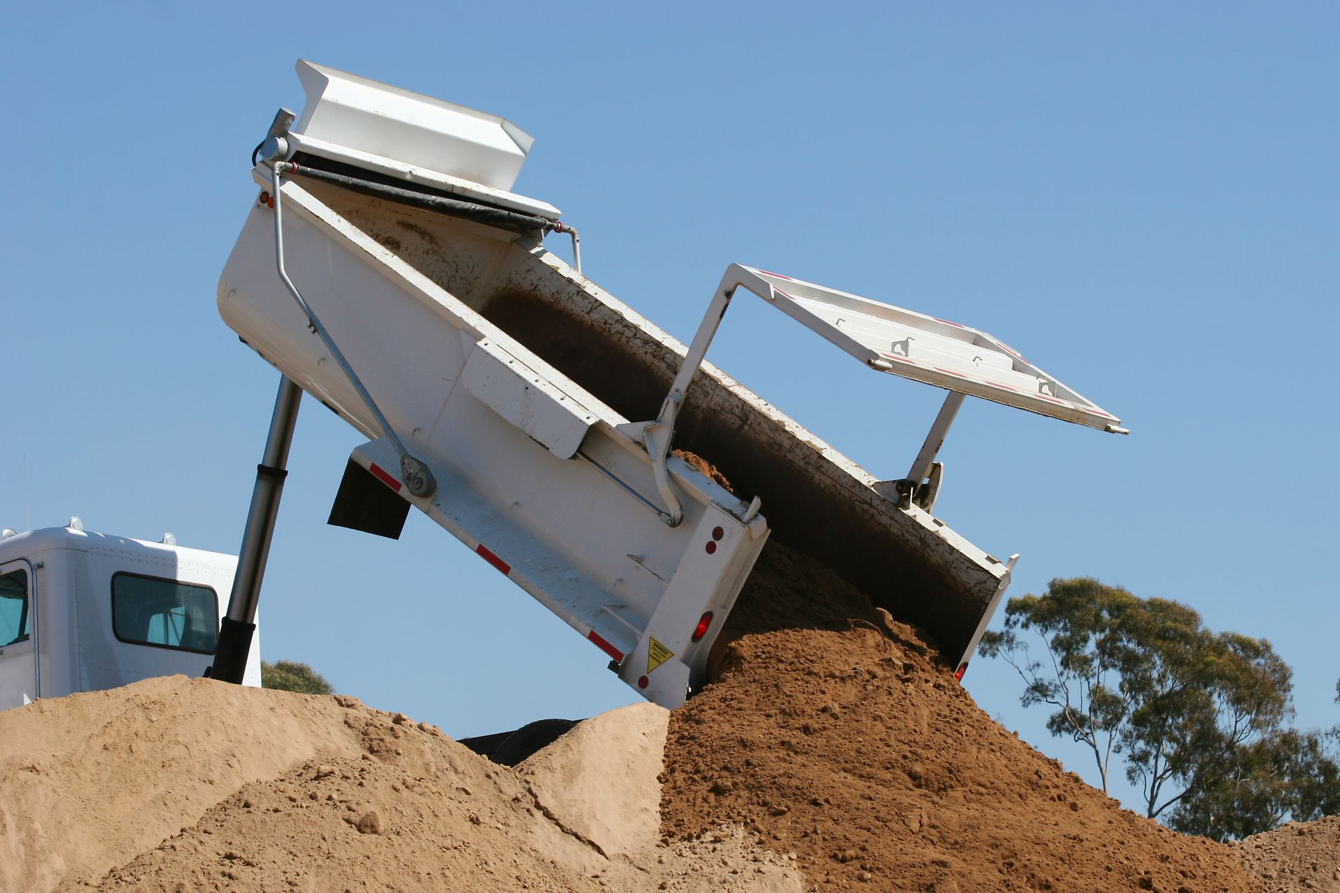 White dump truck unloading a large pile of brown dirt White dump truck unloading a large pile of brown dirt