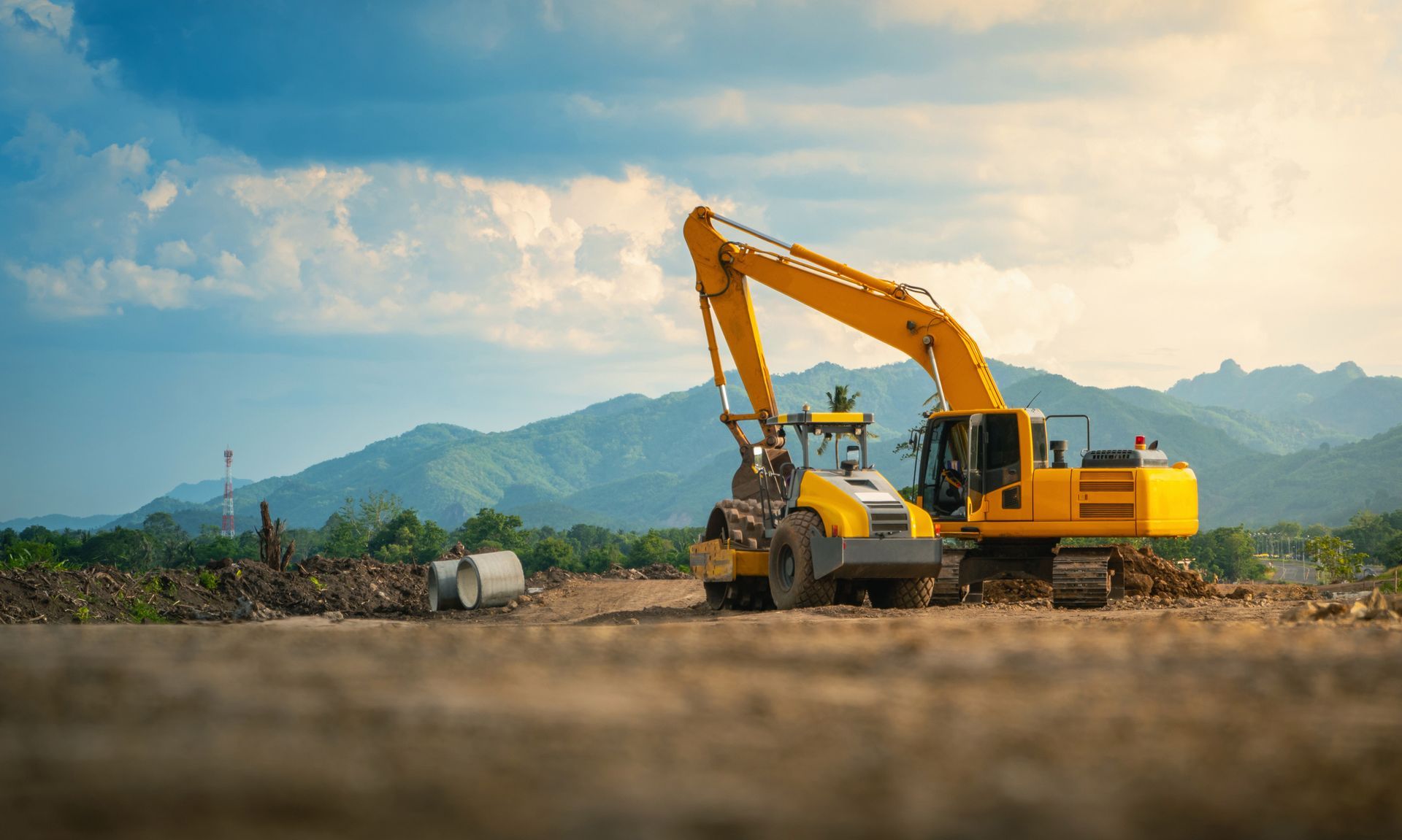Yellow excavator on construction site with mountains in the background under a cloudy sky.