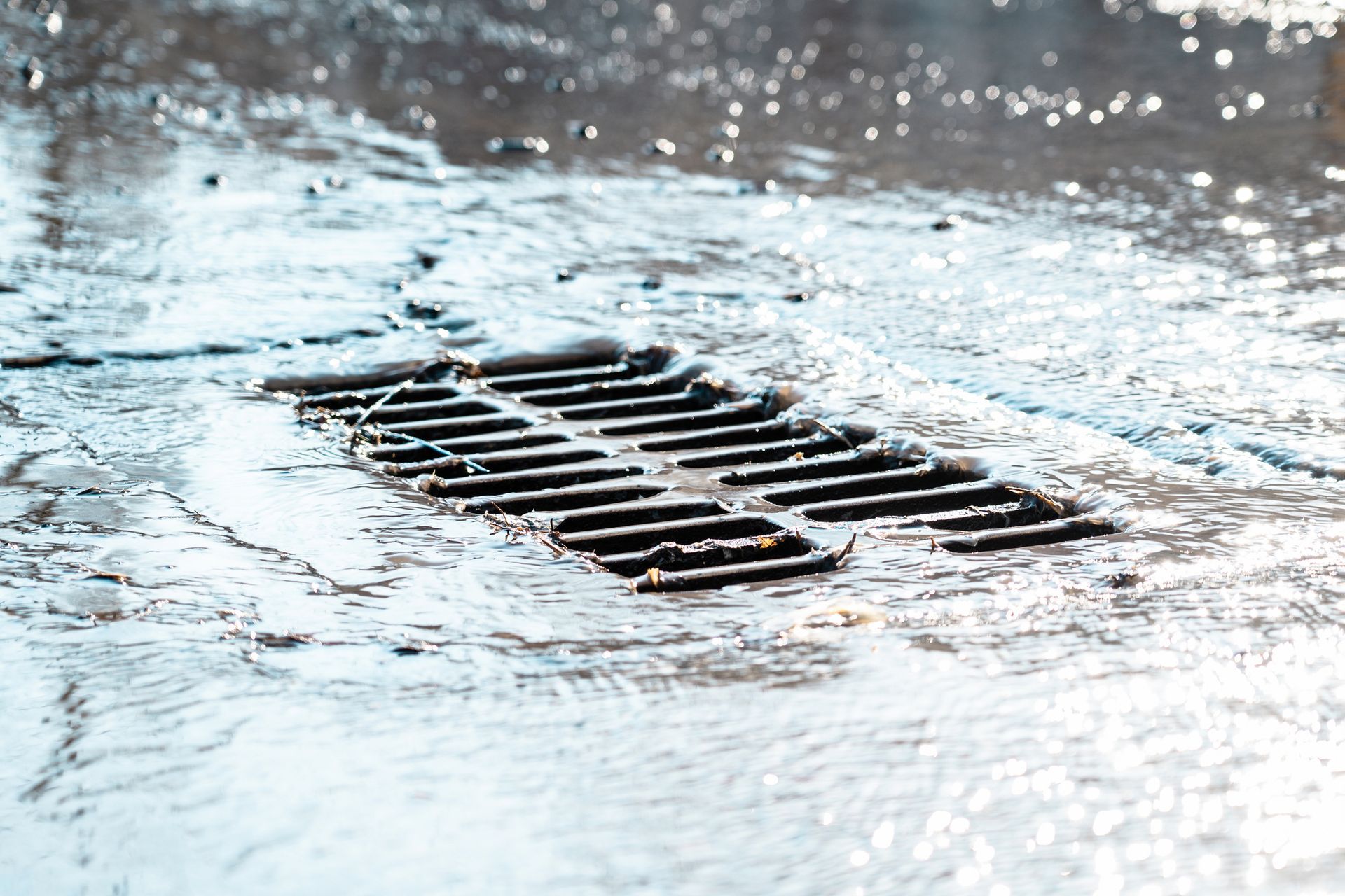 Rainwater flowing over a metal grate in a street, with splashes and reflections.
