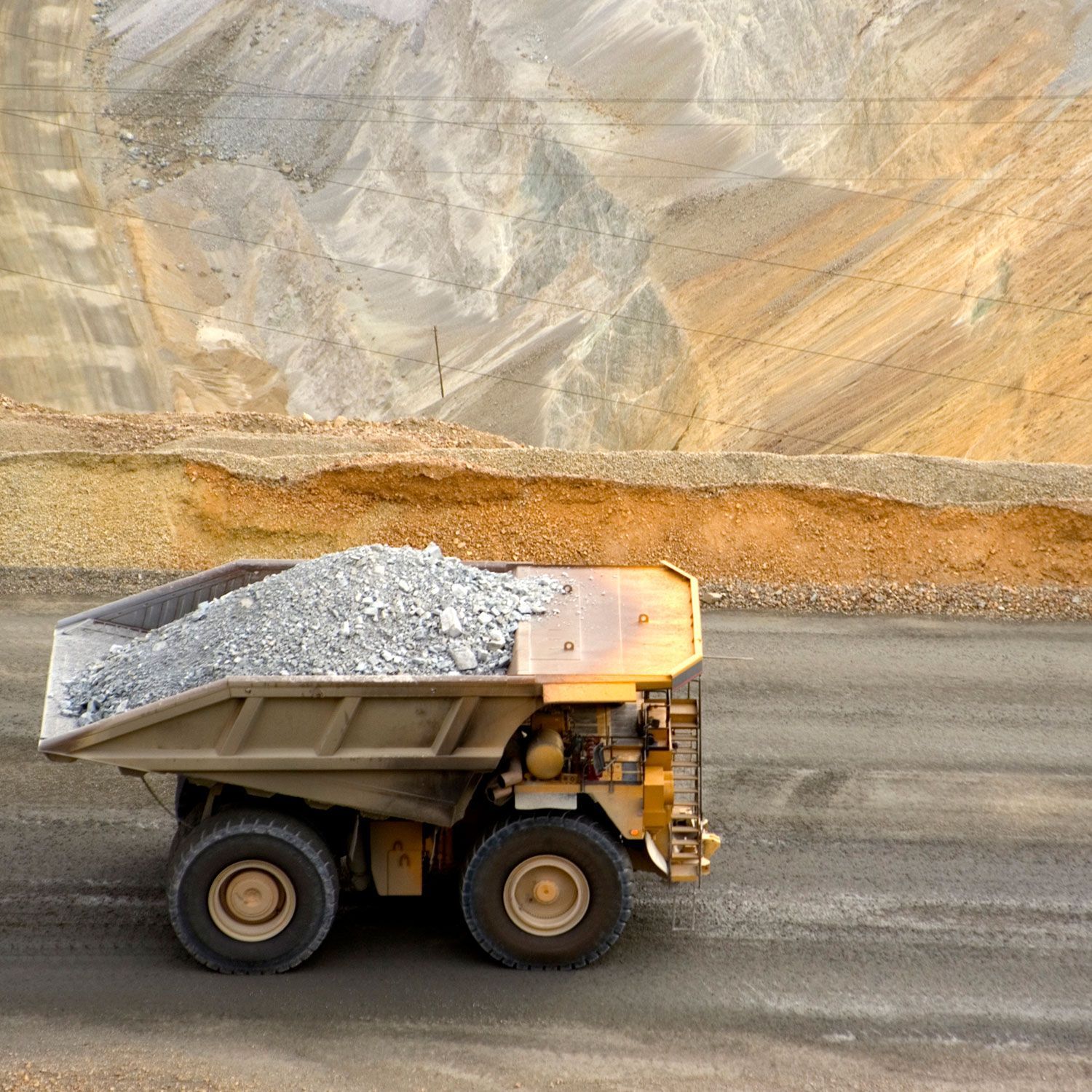 Dump truck loaded with rocks at a mine, with a rocky hillside in the background.