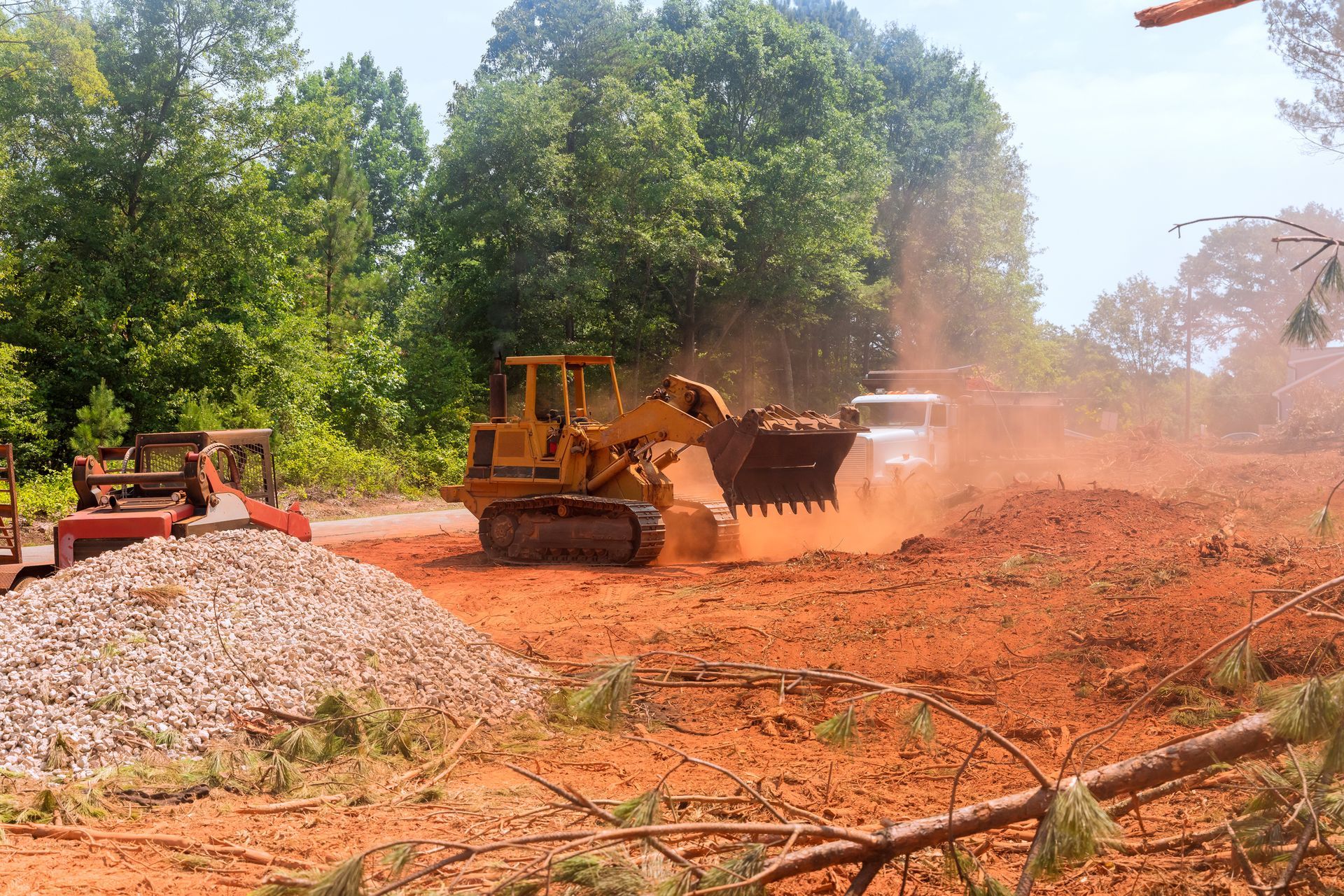 Yellow bulldozer leveling red earth with trees and debris in the background.