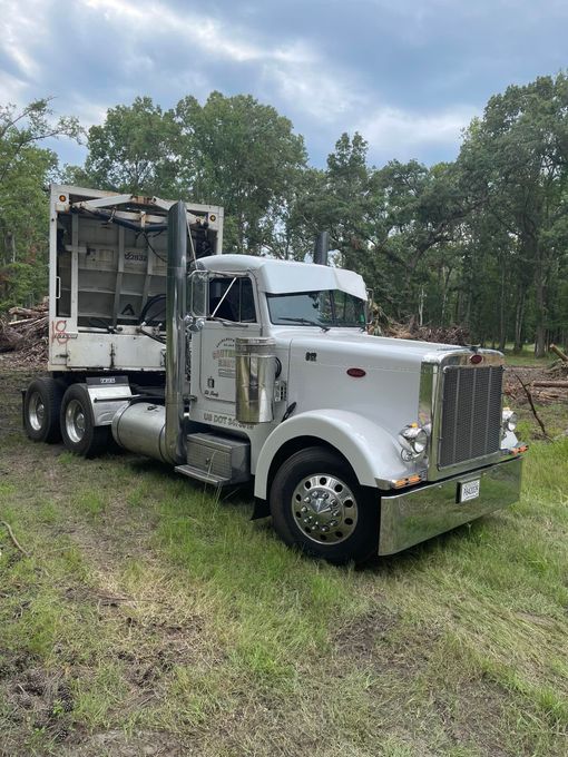 White Peterbilt semi-truck with a flatbed in a grassy area with trees in the background. White Peterbilt semi-truck with a flatbed in a grassy area with trees in the background.