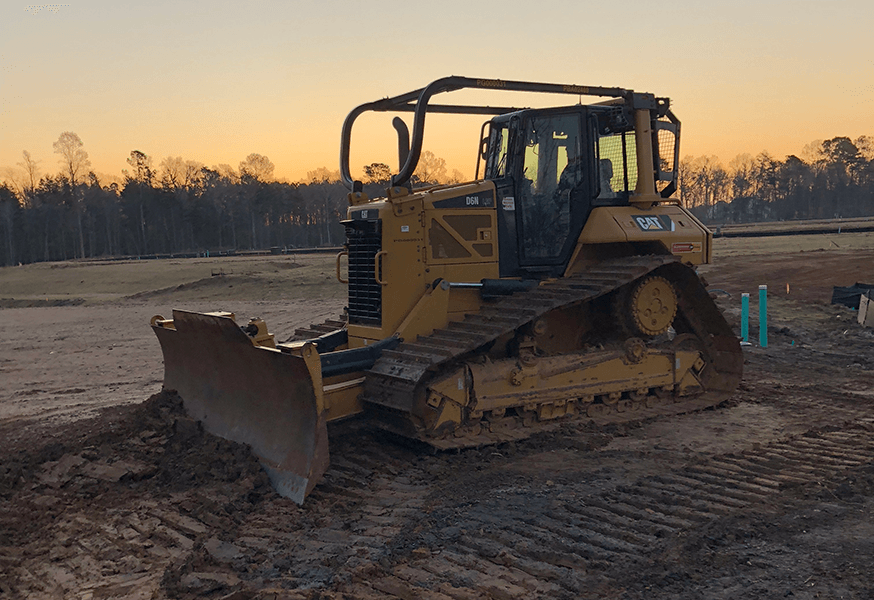Yellow bulldozer on a muddy construction site at sunset, preparing the ground.