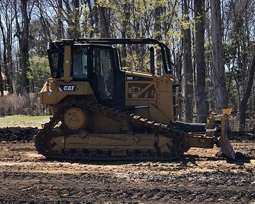 Yellow Caterpillar bulldozer on dirt path near trees.