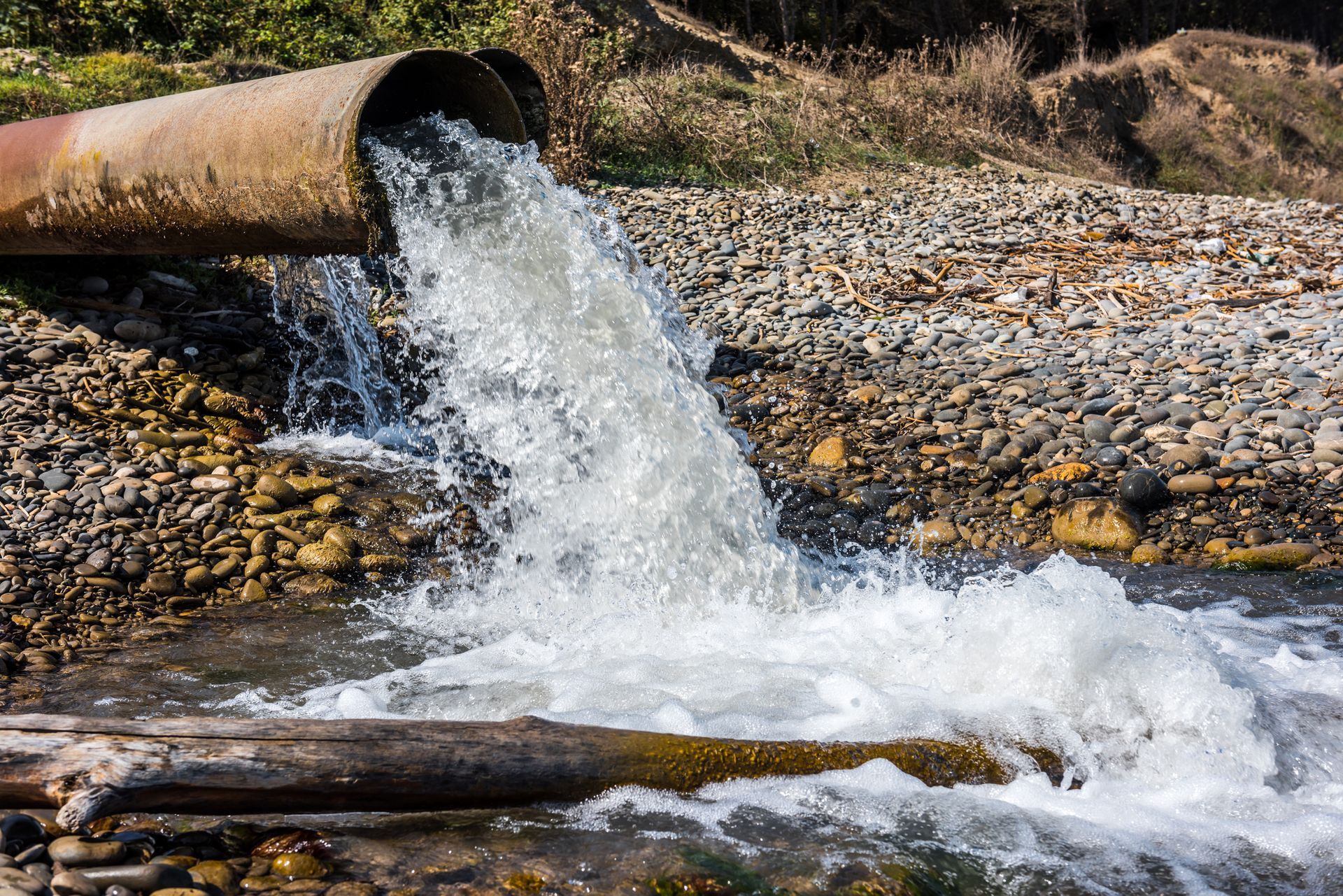 Water gushing from rusty pipe into a rocky stream.