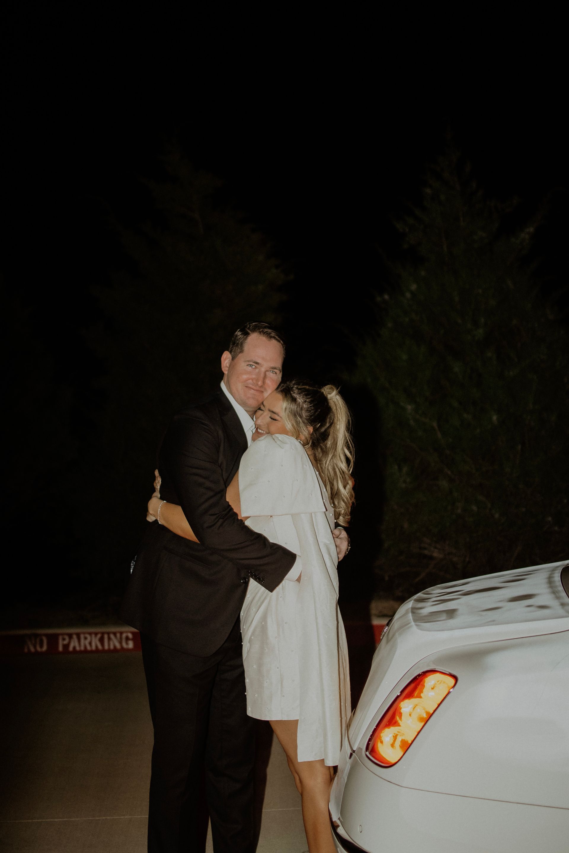 A bride and groom are kissing in front of a white car.