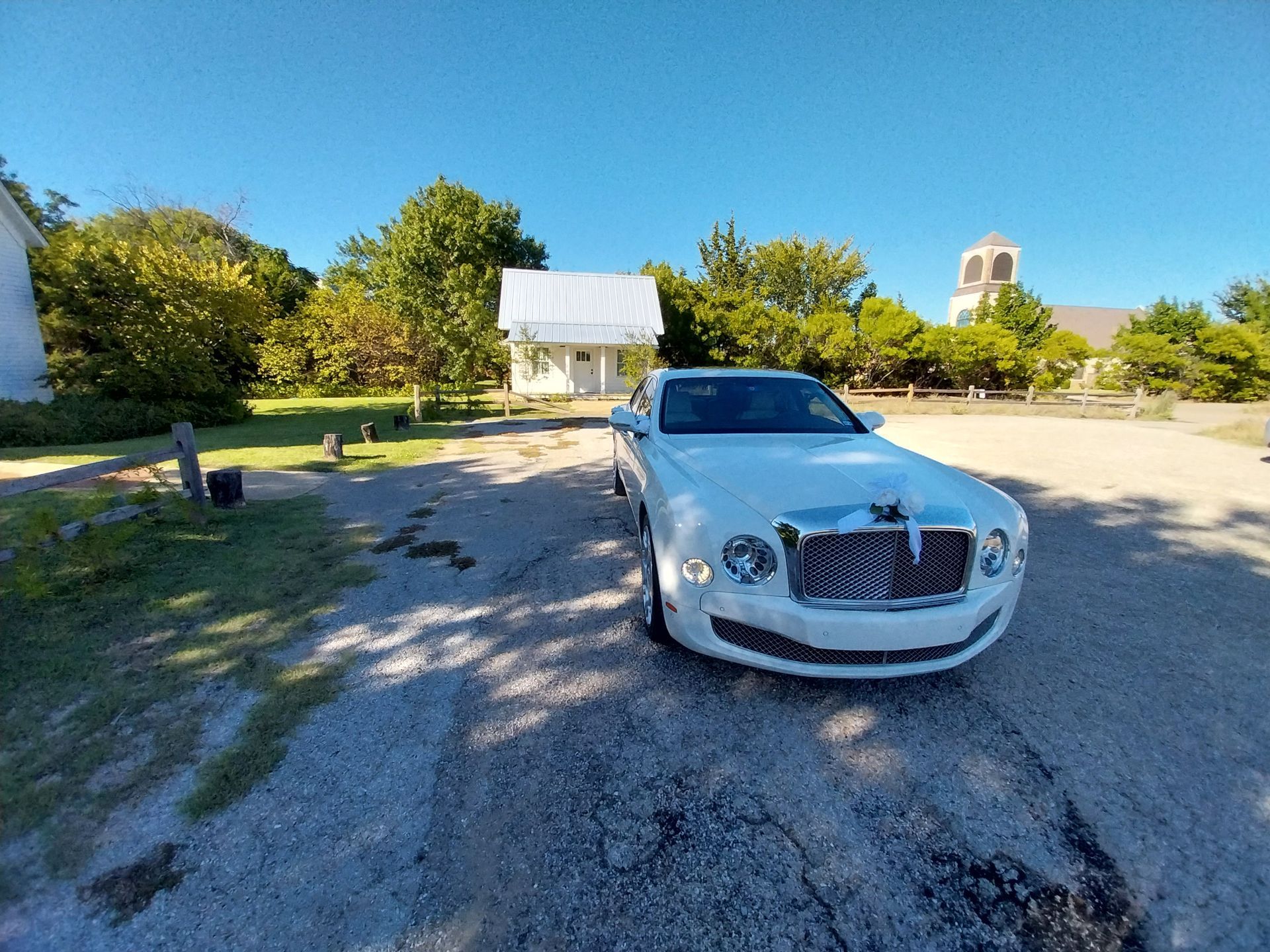A white bentley is parked on the side of a gravel road.