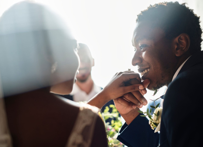 A groom smiles lovingly while kissing his partner's hand during a bright, intimate wedding celebration.