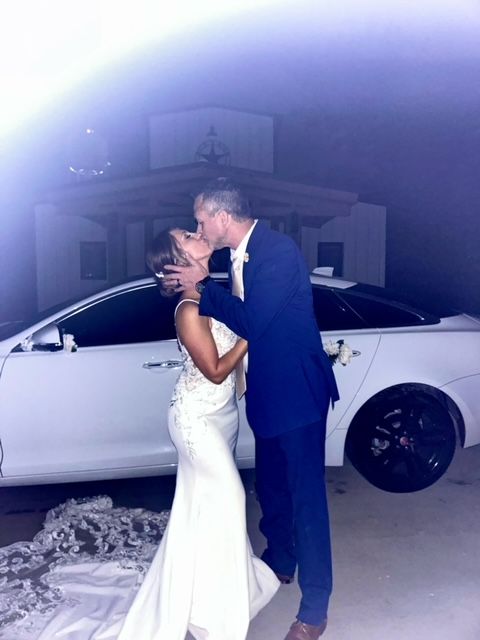 A bride and groom kissing in front of a white car