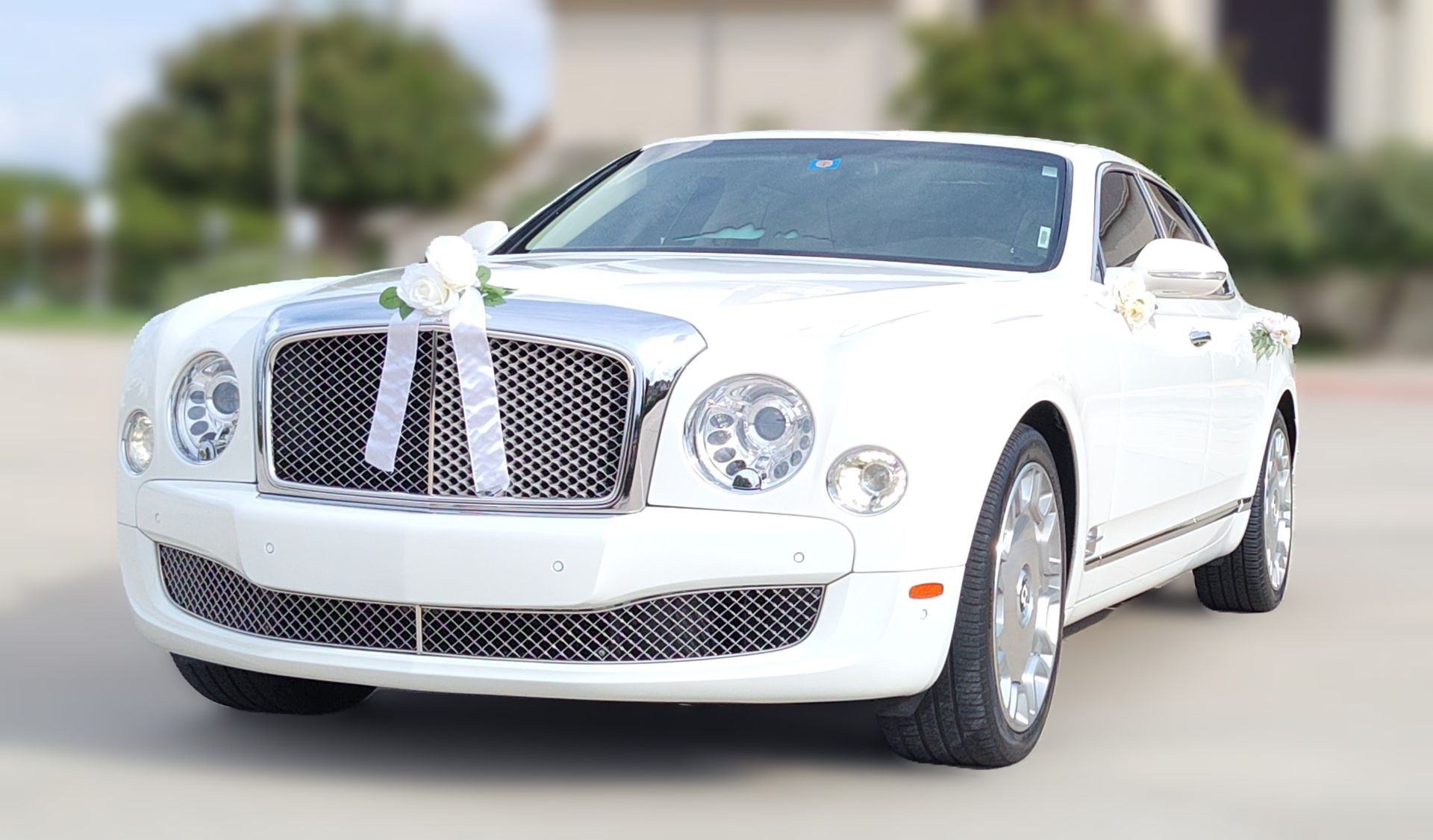 A white bentley with flowers on the hood is parked in a parking lot.