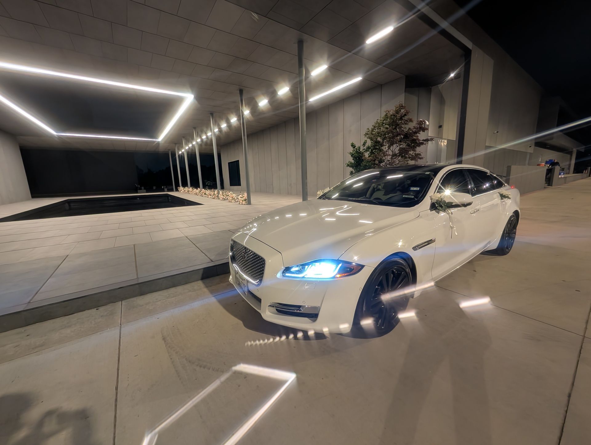 White sedan with blue headlights parked outside a modern building at night