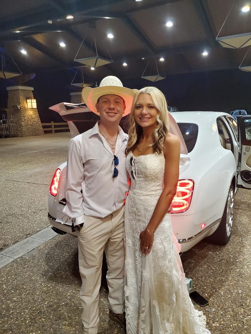 A young couple posing in front of a white limo at night. The man wears a cowboy hat and white outfit.