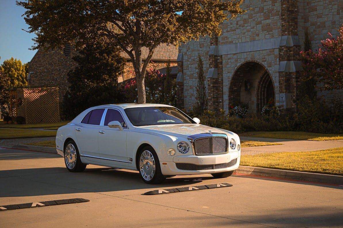 A white car is parked on the side of the road in front of a house.