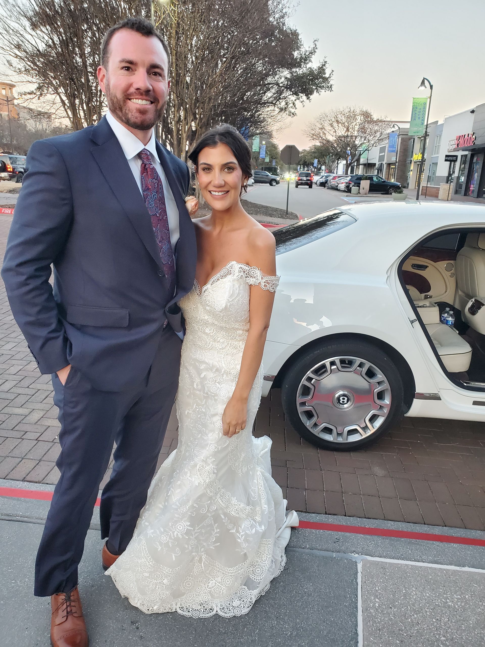 A bride and groom are posing for a picture in front of a white car.