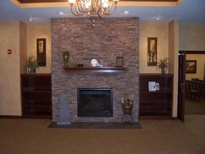 Fireplace with stone facade, dark wood shelves, artwork, and doorway. Brown, tan, and dark tones.