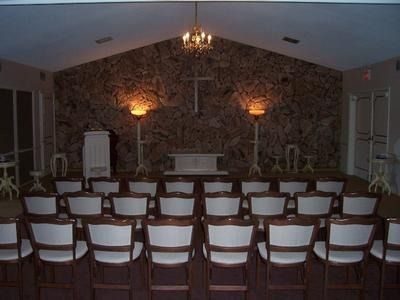 Funeral chapel with chairs facing an altar, cross, and candlelit ambiance.