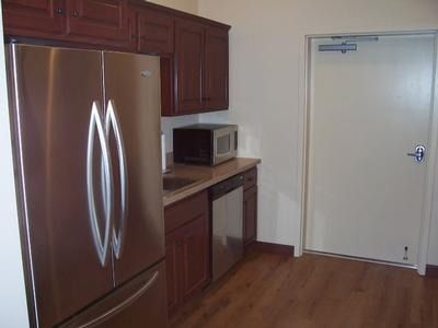 Small kitchen with stainless steel refrigerator, dark wood cabinets, microwave, and door.