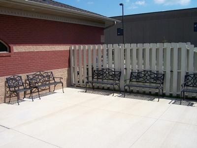 Outdoor patio with benches next to a brick building and a white picket fence under a blue sky.