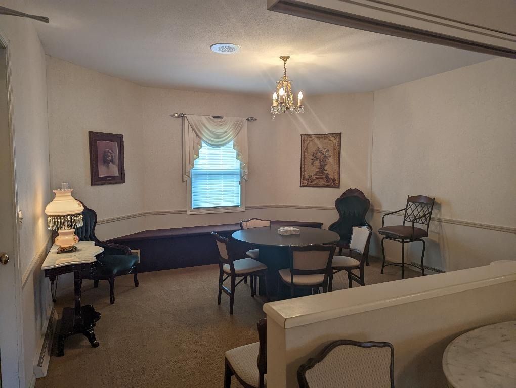 A room with a round table, chairs, and a window with a valance; chandelier overhead.