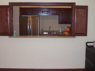 A pass-through kitchen area with dark brown cabinets, a stainless steel refrigerator, and granite countertop.