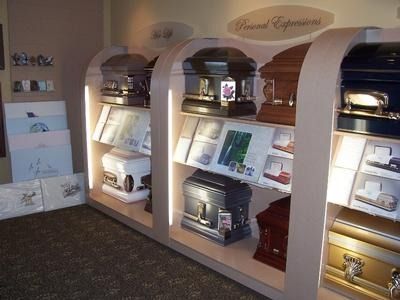 Casket display in a funeral home showroom. Various caskets and memorial service brochures are showcased on shelves.