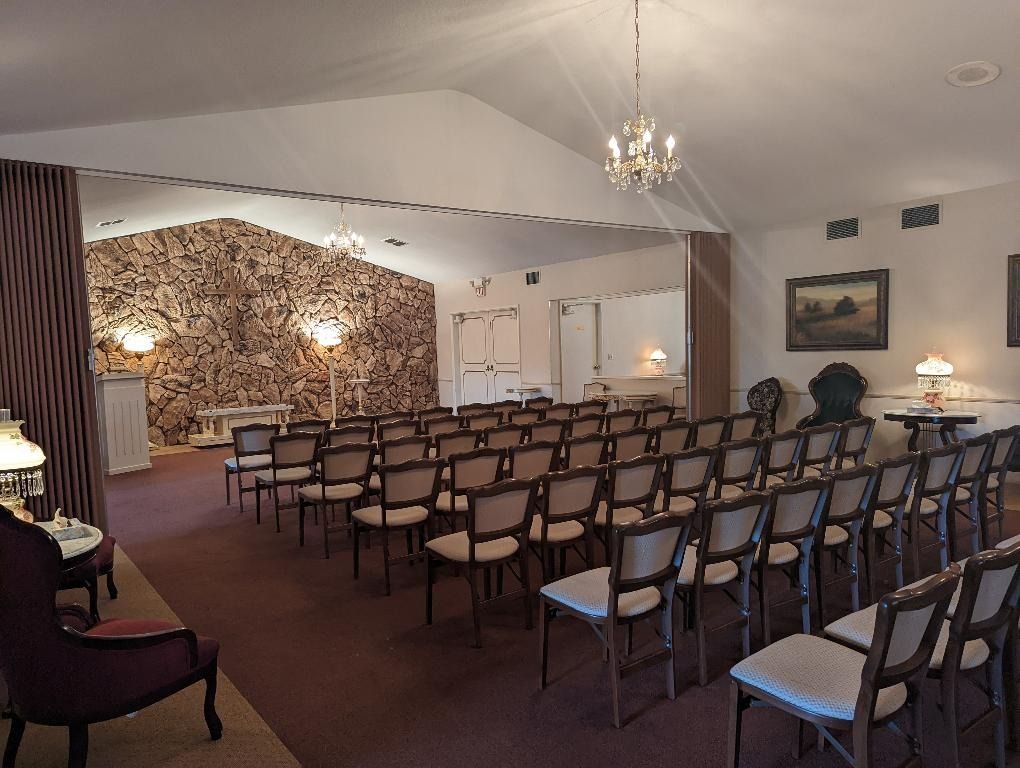 Rows of chairs face a textured wall in a formal room, possibly a chapel or funeral home.