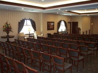 Rows of empty chairs face a small stage in a room with windows and decorative accents.