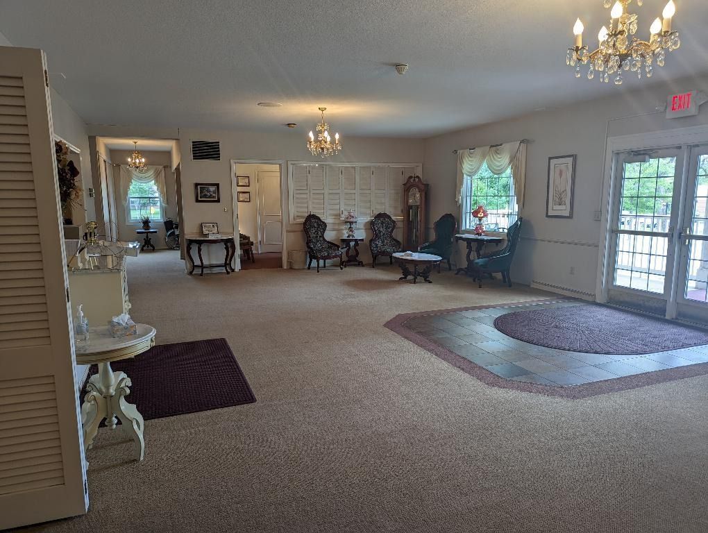 Spacious, carpeted room with multiple chandeliers, seating areas, and an exit door; likely a waiting room.